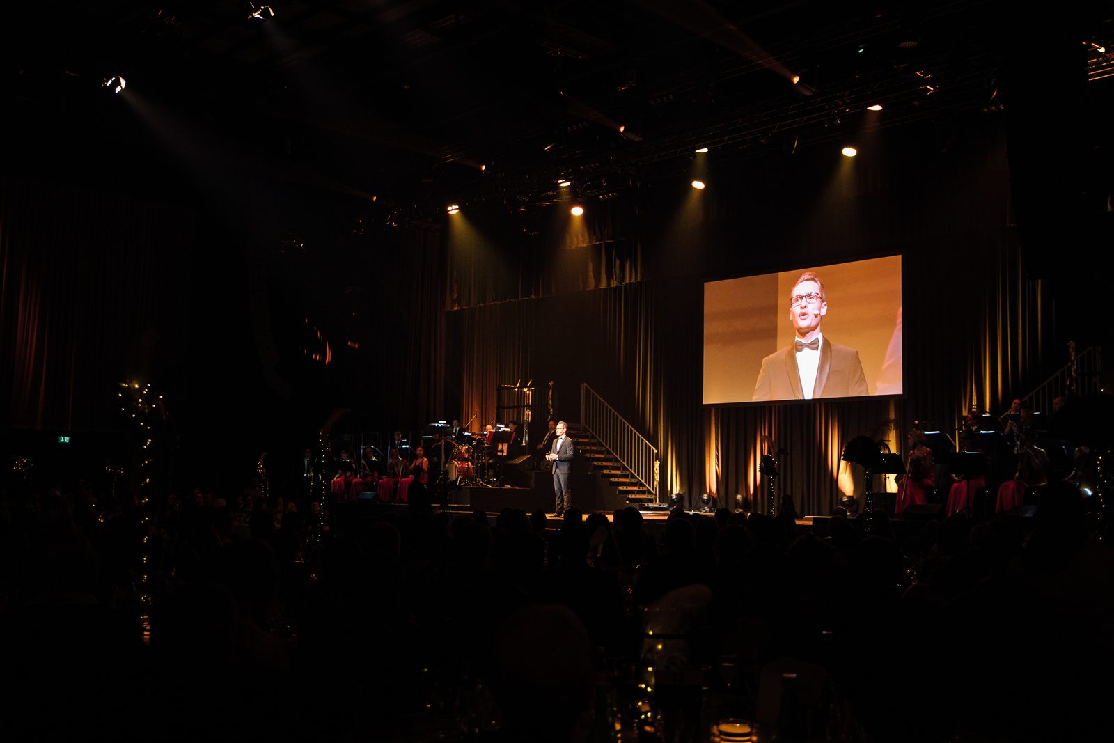 Gala-Abend, dunkler Saal mit Buehne und Grossleinwand